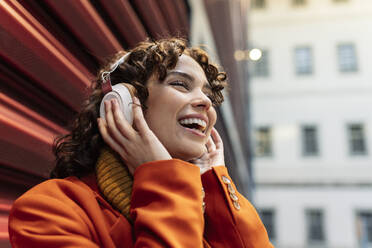 Cheerful woman listening music through headphones near wall - JCCMF05428