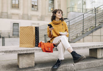 Junge Frau mit Smartphone und Essensschale auf einer Betonbank sitzend - JCCMF05445