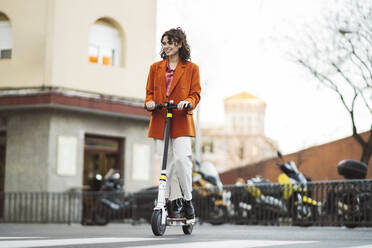 Young woman riding electric push scooter on footpath in city - JCCMF05460