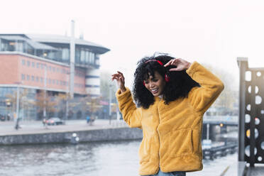 Happy woman listening music through headphones by canal in city - PNAF03273