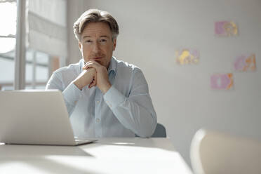 Businessman with hand on chin sitting at desk - KNSF09244