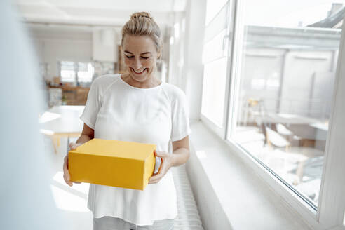 Cheerful businesswoman standing with box in office - KNSF09247