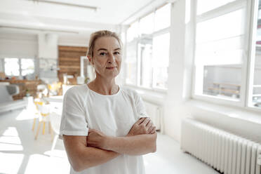 Smiling businesswoman standing with arms crossed in office - KNSF09253