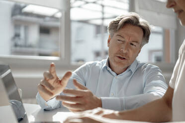 Businessman discussing with businesswoman sitting at desk in office - KNSF09282