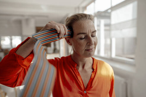 Geschäftsfrau mit geschlossenen Augen berührt Computerkabel am Kopf im Büro - KNSF09288