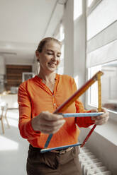 Lächelnde Geschäftsfrau macht Hausform mit Lineal im Büro - KNSF09292