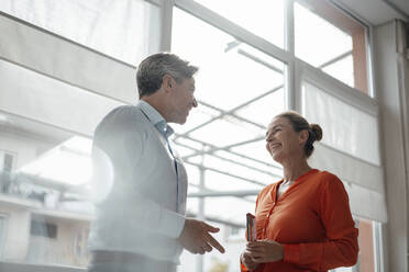 Happy businesswoman with businessman standing in front of window at office - KNSF09296