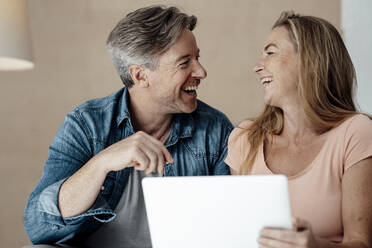 Fröhliche Frau und Mann sitzen mit Laptop zu Hause - KNSF09325