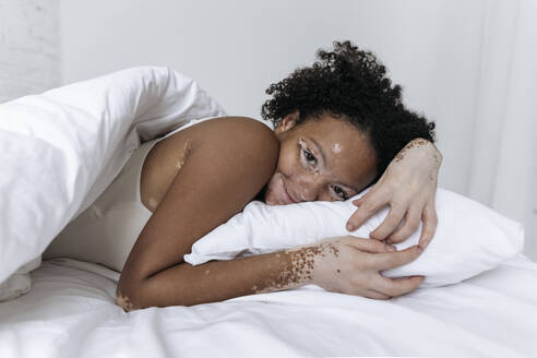 Lächelnde Frau mit schwarzen Haaren ruht sich zu Hause auf dem Bett aus - SIF00015