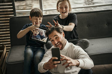 Verspielter Mann mit Söhnen nimmt Selfie durch Smartphone zu Hause - MJRF00616