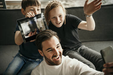 Happy man with sons taking selfie through mobile phone at home - MJRF00617