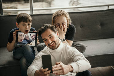 Glücklicher Mann nimmt Selfie durch Smartphone mit Söhnen machen Gesichter zu Hause - MJRF00618