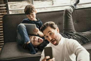 Man sticking out tongue taking selfie with sons making faces at home - MJRF00619