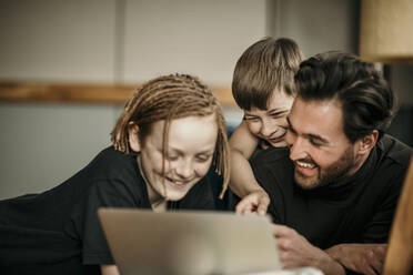 Fröhliche Jungen mit Vater, die zu Hause einen Laptop benutzen - MJRF00623