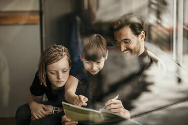 Lächelnder Vater erklärt den Söhnen das Lernen zu Hause - MJRF00626