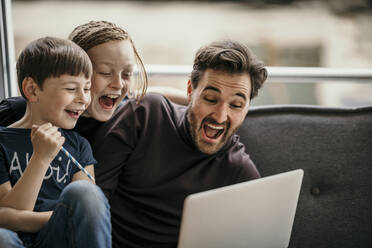 Fröhliche Jungen mit Vater, der einen Laptop benutzt und sich zu Hause amüsiert - MJRF00638