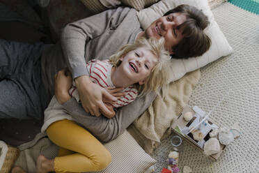 Happy father lying with daughter on pillows at home - TYF00108