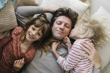 Happy father lying with daughters on pillows at home - TYF00109