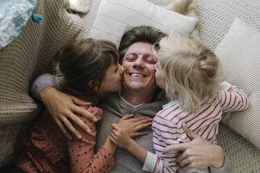 Daughters kissing father lying on pillow at home - TYF00110