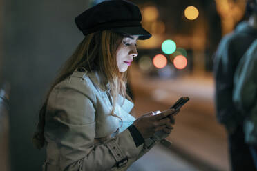 Woman wearing cap using mobile phone at night - JSRF01875