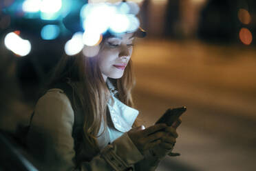 Beautiful woman wearing cap using mobile phone at night - JSRF01876