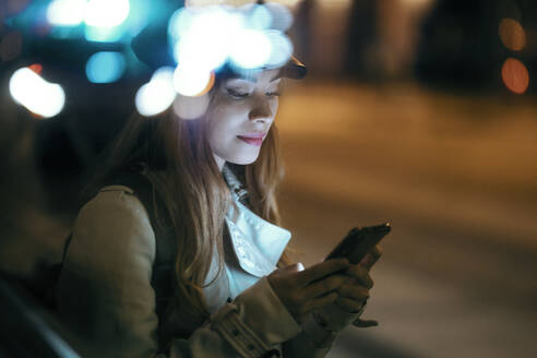 Schöne Frau mit Mütze, die nachts ein Mobiltelefon benutzt - JSRF01876