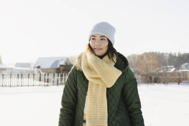 Woman wearing knit hat and scarf standing at snowy garden - SEAF00543