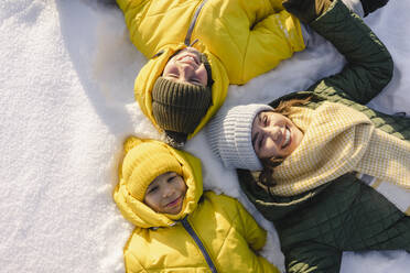 Lächelnde Mutter mit Söhnen, die im verschneiten Garten liegen - SEAF00544