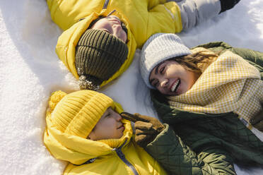 Glückliche Mutter berührt die Nase eines Jungen, der im Winter im Schnee liegt - SEAF00546