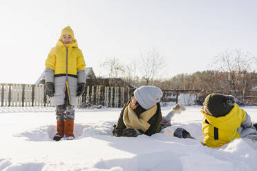 Frau mit Sohn im Schnee liegend mit Blick auf den im Winter stehenden Jungen - SEAF00549