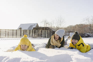 Verspielte Jungen mit Mutter im Schnee liegend im Winter - SEAF00550