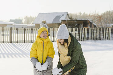 Playful woman with son holding snow in winter - SEAF00552