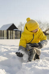 Glücklicher Junge mit Strickmütze, der im Winter mit Schnee spielt - SEAF00557