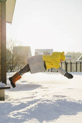 Verspielter Junge springt im Winter im Garten in den tiefen Schnee - SEAF00565