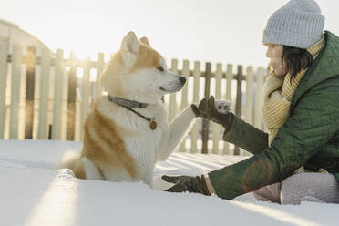 Woman holding dog paw sitting on deep snow in winter - SEAF00568