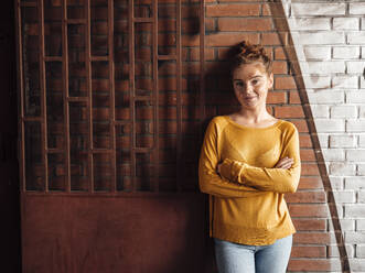 Young woman with arms crossed in front of brick wall - JOSEF07203