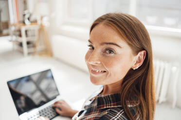 Smiling woman with laptop at home - JOSEF07210