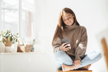 Lächelnde Textnachrichten auf dem Mobiltelefon zu Hause - JOSEF07213