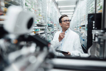 Pharmacist with tablet PC checking medicine on rack and taking inventory in storage room - JOSEF07262