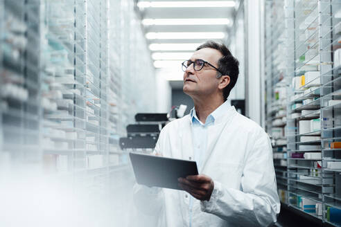 Pharmacist with tablet PC checking medicines on shelf and taking inventory in pharmacy - JOSEF07263