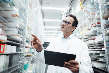 Pharmacist with tablet PC checking medicines on rack and taking inventory in storage room - JOSEF07265