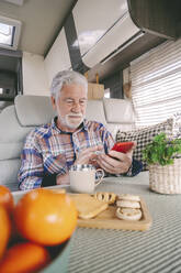 Älterer Mann mit Frühstück und Smartphone im Wohnmobil - SIPF02744