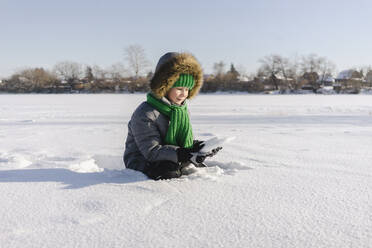 Boy with warm clothing sitting in snow - SEAF00594