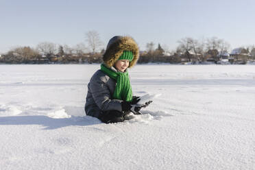 Junge mit warmer Kleidung im Schnee sitzend - SEAF00594