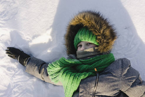 Junge in warmer Kleidung auf Schnee liegend - SEAF00605