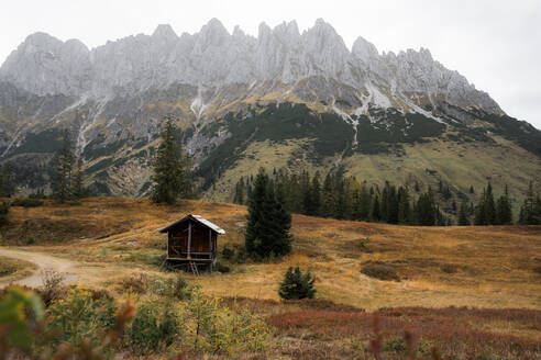 Small wooden cabin located on grassy slope of mountain in autumn misty weather in Austria - ADSF33659