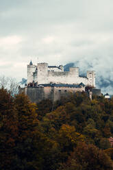 Drone view of aged stone castle located in hilly terrain covered with lush coniferous woods in Salzburg City in Austria - ADSF33661