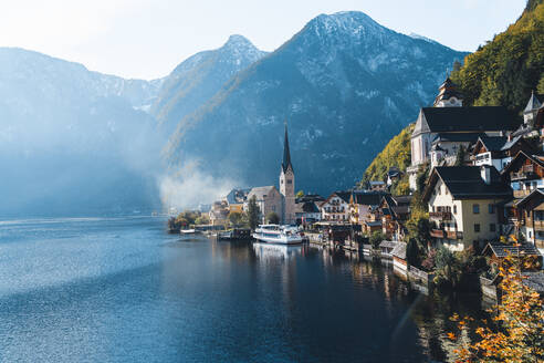 Malerischer Blick auf ein kleines Dorf in der Nähe eines ruhigen Sees, umgeben von hohen Bergen mit Nadelwäldern, an einem sonnigen Herbsttag in Österreich bei Salzburg - ADSF33668