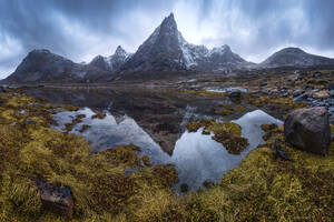 Sea water flowing in archipelago against overcast sky and rough mountain ridge with snowy peaks in Norway - ADSF33703