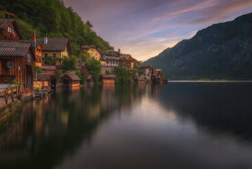 Hallstatt Dorf mit Wohngebäuden am Ufer in der Nähe von grünen Bäumen und ruhigem Wasser gegen Bergkamm in Österreich am Sommertag gelegen - ADSF33713